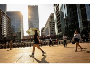 A pedestrian uses a umbrella to protect herself from the sun, at Canary Wharf, during a heatwave in London, UK, on Monday, July 18, 2022. Extreme heat could lead to power outages, canceled flights and may be a danger to life while the so-called Red Extreme warning is in place across parts of southern England on Monday and Tuesday. Photographer: Jose Sarmento Matos/Bloomberg