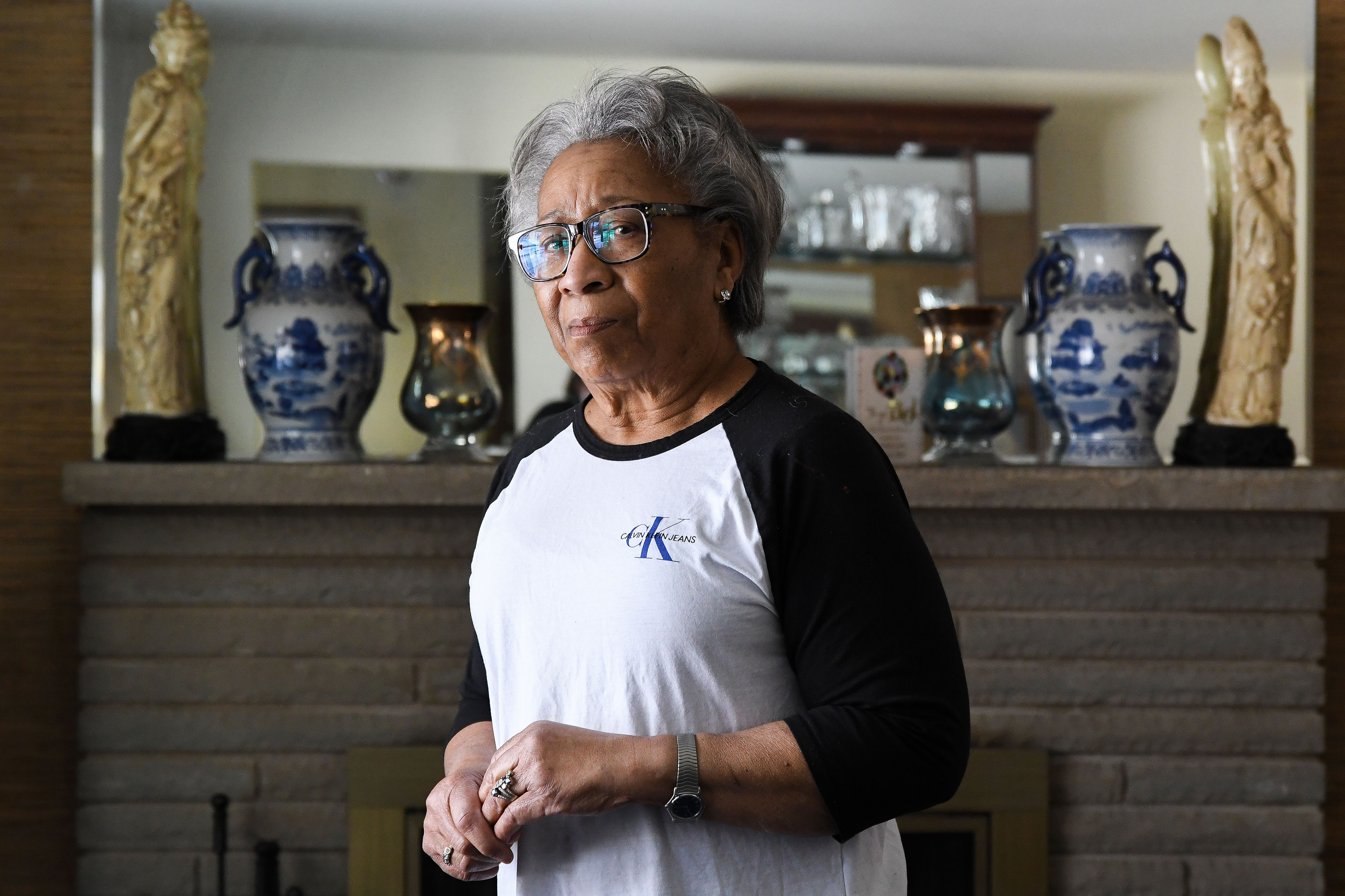 A woman standing in front of a fireplace looks at the camera.