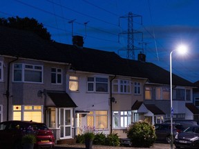 An electricity transmission tower near residential houses with lights on in Upminster, UK, on Monday, July 4, 2022. The UK is set to water down one of its key climate change policies as it battles soaring energy prices that have contributed to a cost-of-living crisis for millions of consumers. Photographer: Chris Ratcliffe/Bloomberg